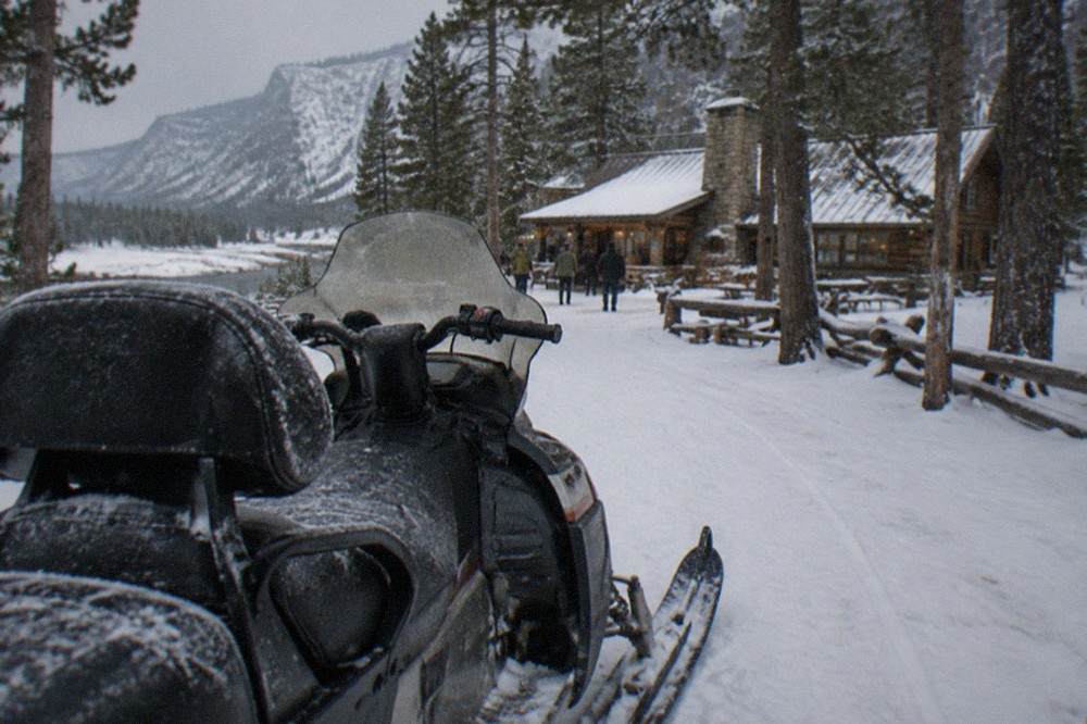 Long-seat touring snowmobile with rear backrest and handgrips parked beside a groomed forest trail