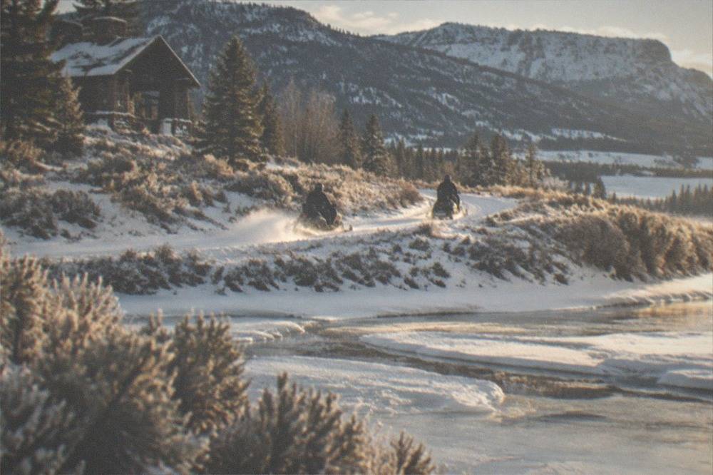 Pair of snowmobiles traveling single file along a groomed road beside a snow-covered river valley