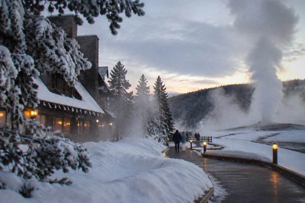 Steam rising from the boardwalk around Old Faithful with snow banks and frost-covered trees in the background