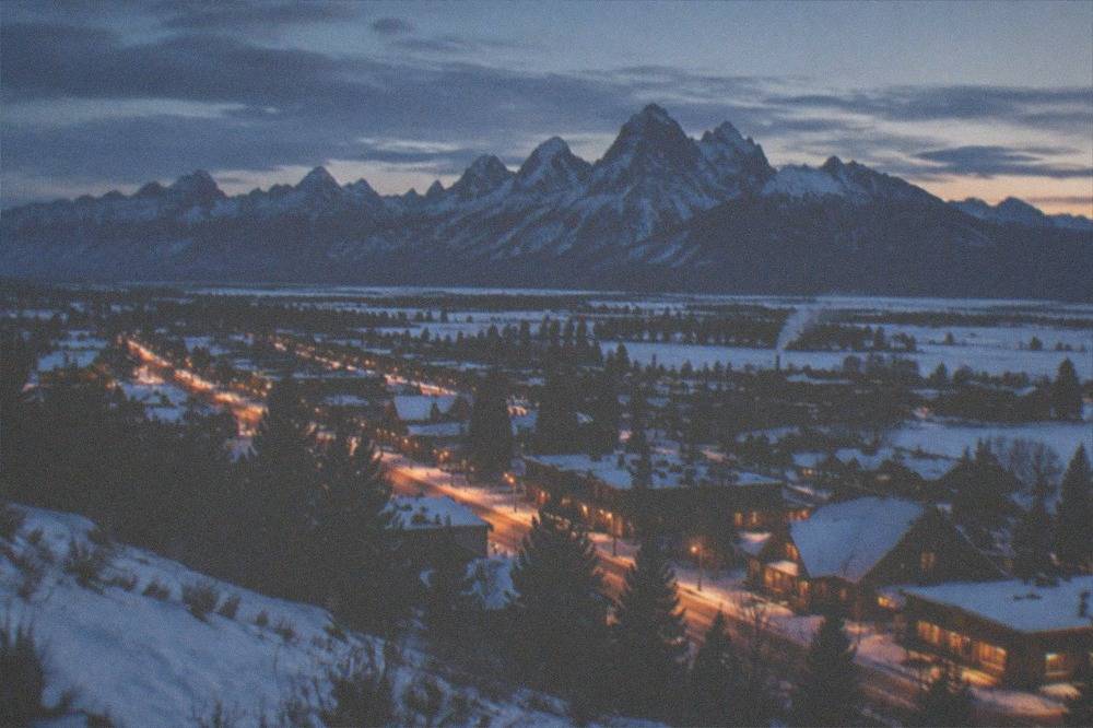 Snowy mountain valley at dusk with town lights glowing along a main street