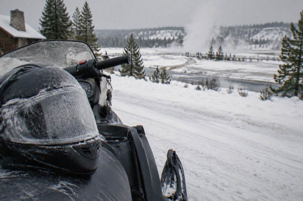 Frost-covered snowmobile helmet resting on a sled seat beside a snowy forest road