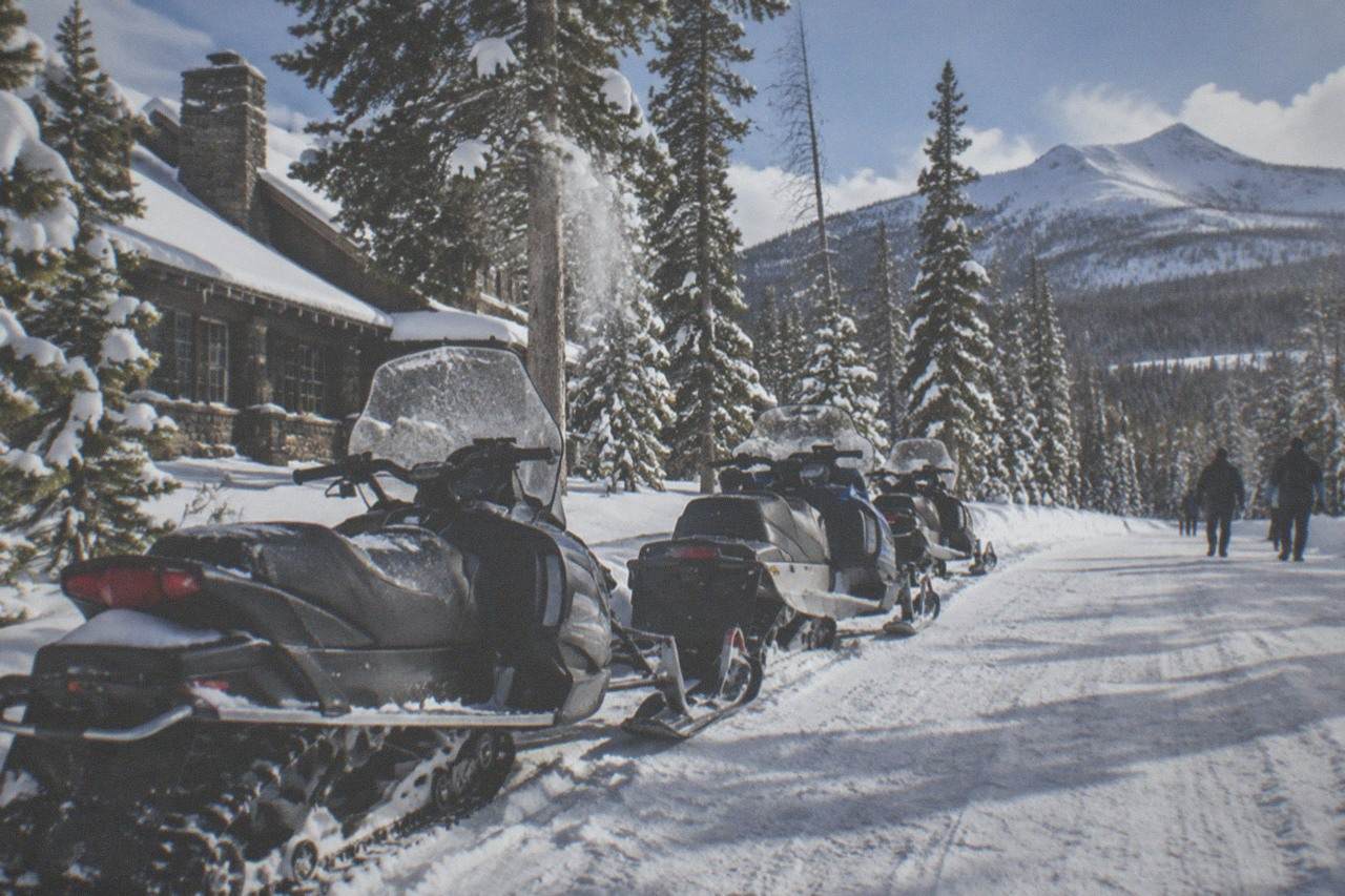 A row of parked snowmobiles on a groomed winter road in Yellowstone with snow-covered trees.