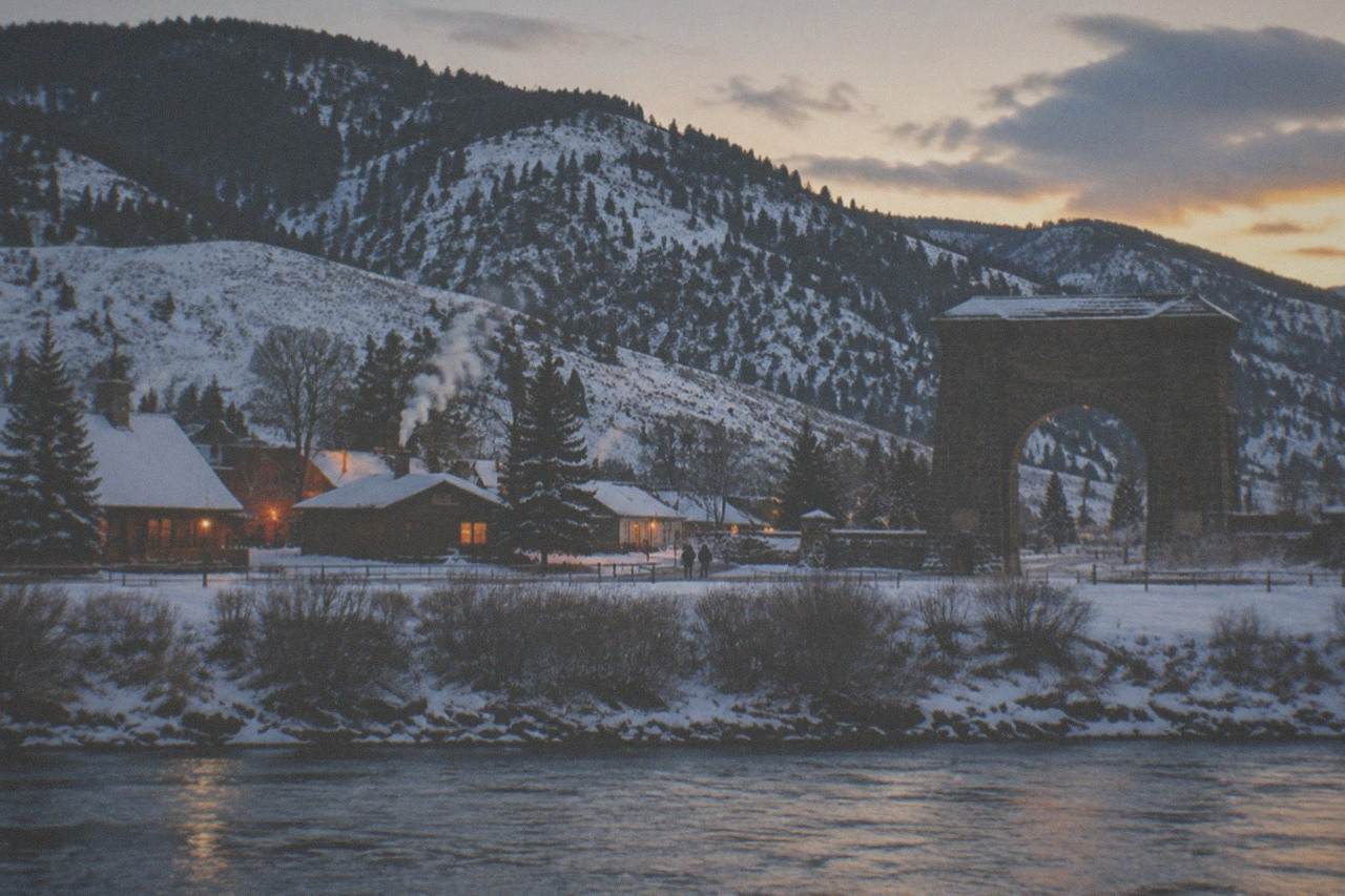 Snow-covered gateway town at dusk with warm lights in windows and mountains behind
