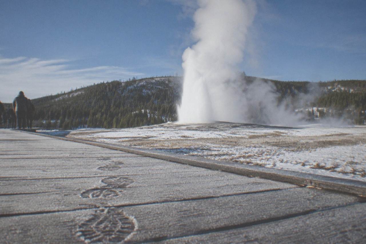 A snow-covered boardwalk at Old Faithful with steam rising into the crisp winter air