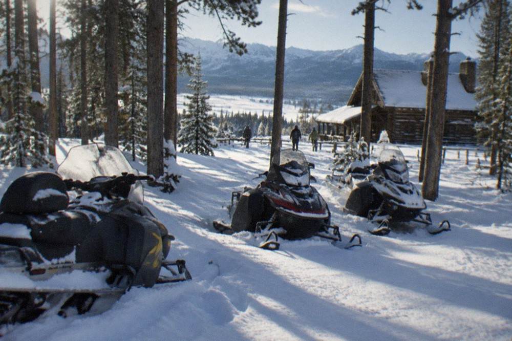 Snowmobiles parked in a snowy forest clearing with tall pines and deep drifts