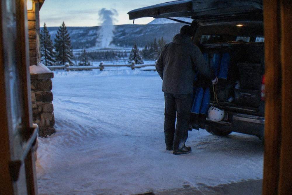 Guide handing helmets and insulated suits to riders beside a parked van in snow