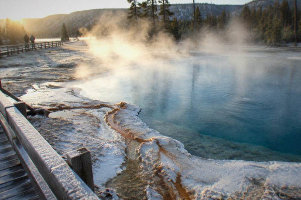Steam rising from geothermal pools beside a snow-covered boardwalk in winter