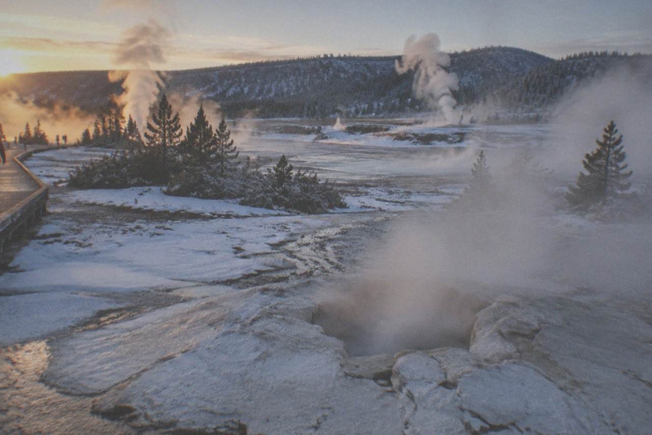 Steam rising from geysers across a snow-covered valley at dawn