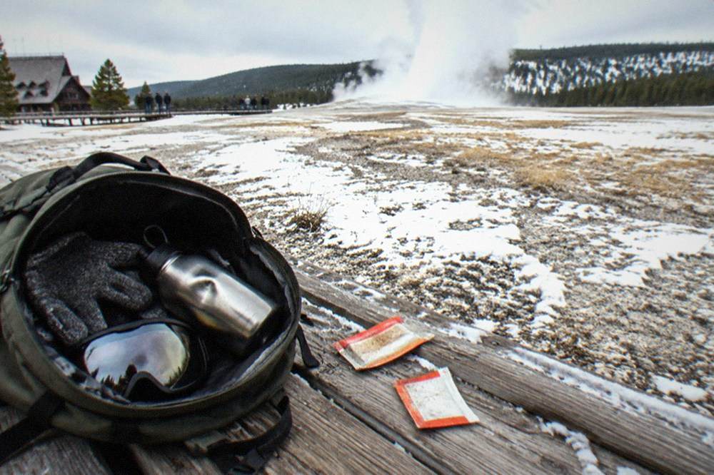Small winter daypack with gloves, goggles, water bottle, and hand warmers packed on a snowy surface