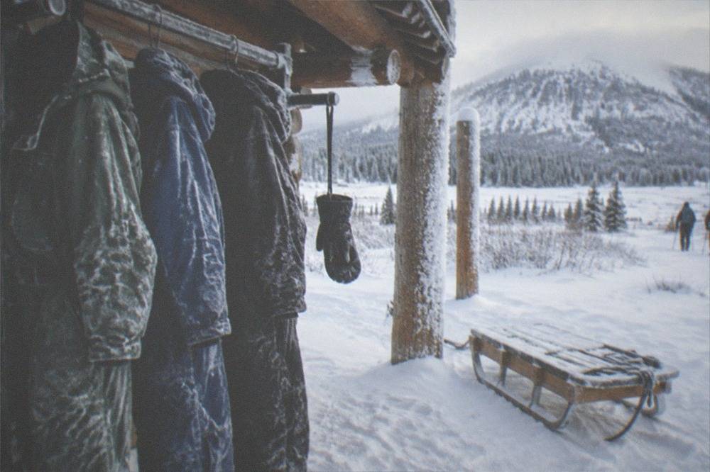 insulated snowmobile suits and helmets hung on a rack beside a snow-dusted sled