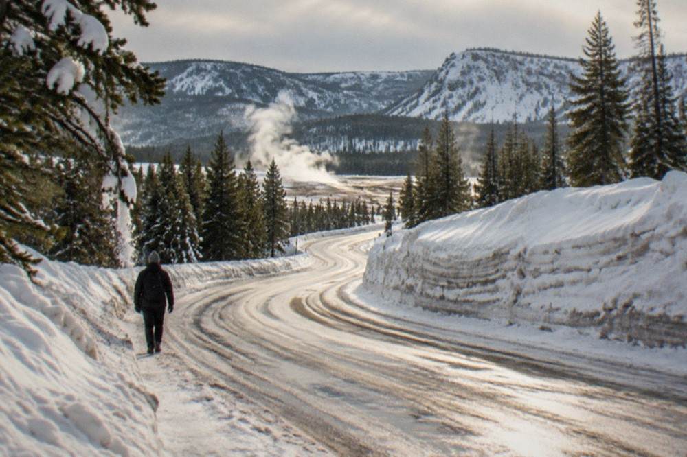 Groomed snow road winding between snow-laden evergreens toward distant mountains