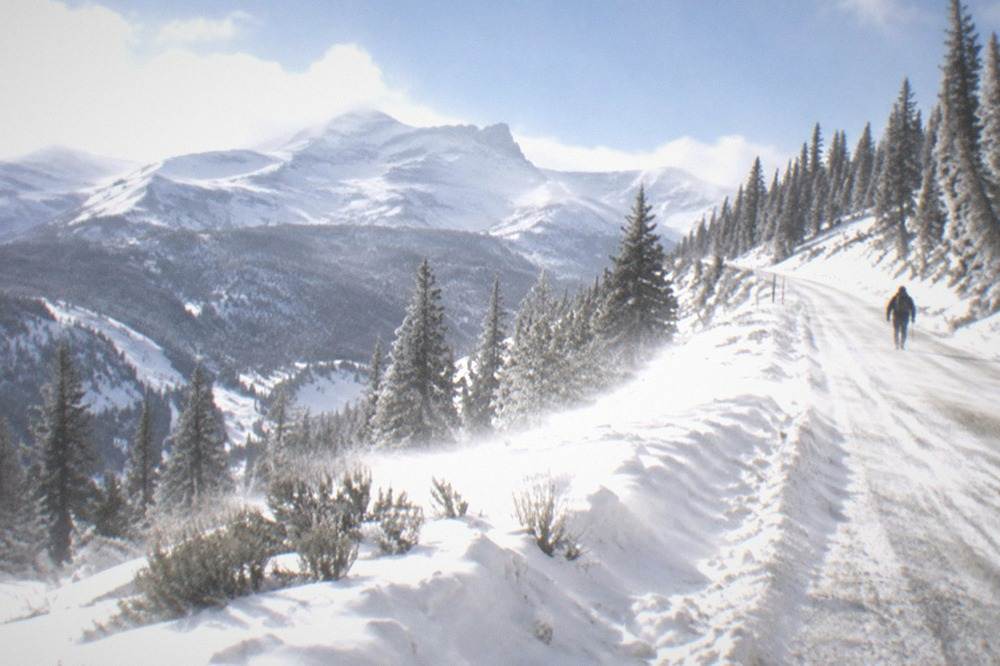 Snowy mountain pass road with warning signs and wind-scoured drifts along the shoulders