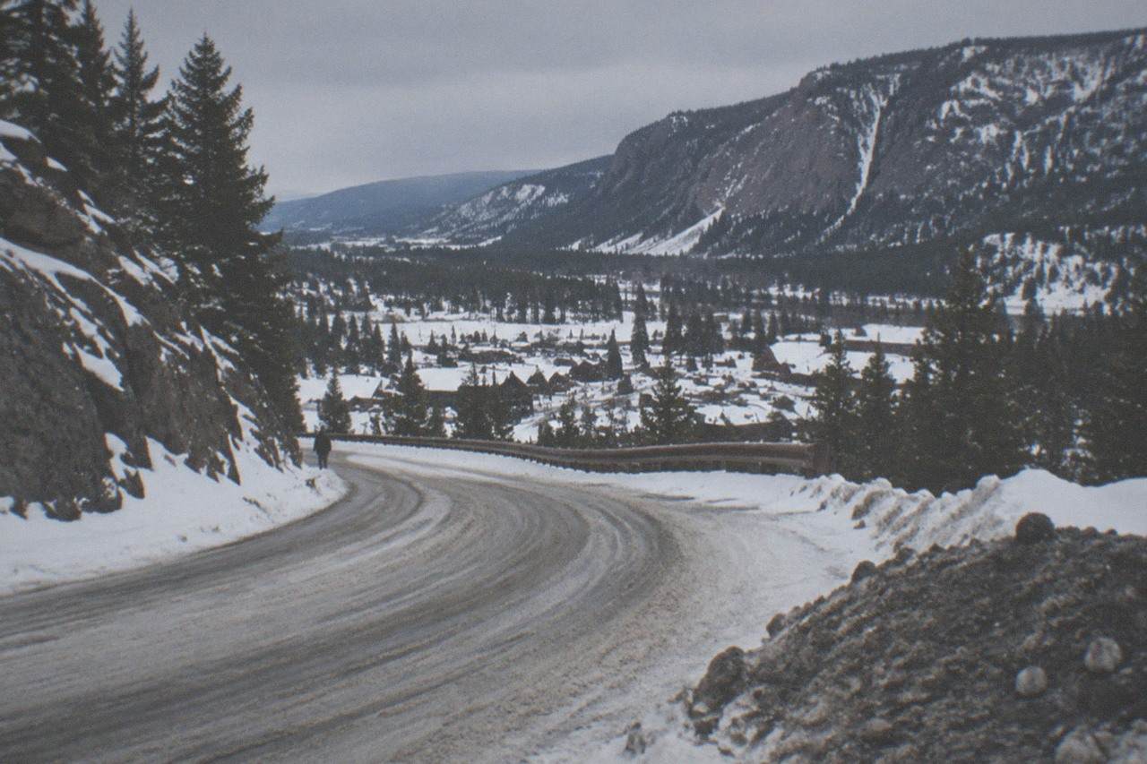 Snow-covered road winding through a mountain canyon toward a small town under gray winter sky