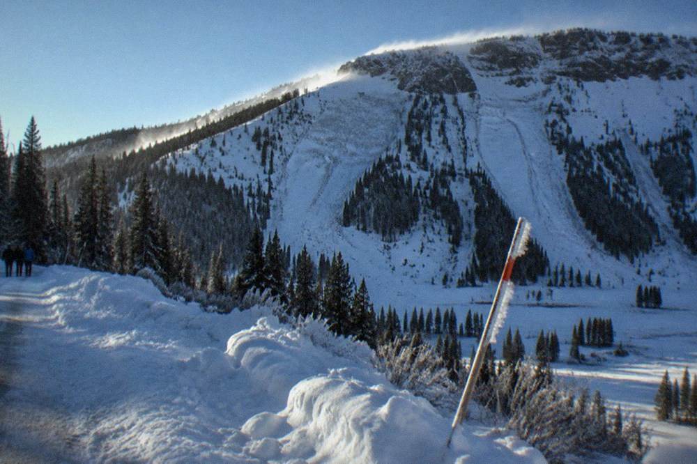 Steep snow-laden mountain slope above a narrow winter road with wind-scoured ridgeline