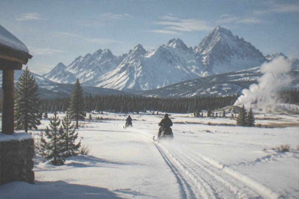 Snowmobile tracks crossing a wide snowy valley with jagged white peaks rising behind