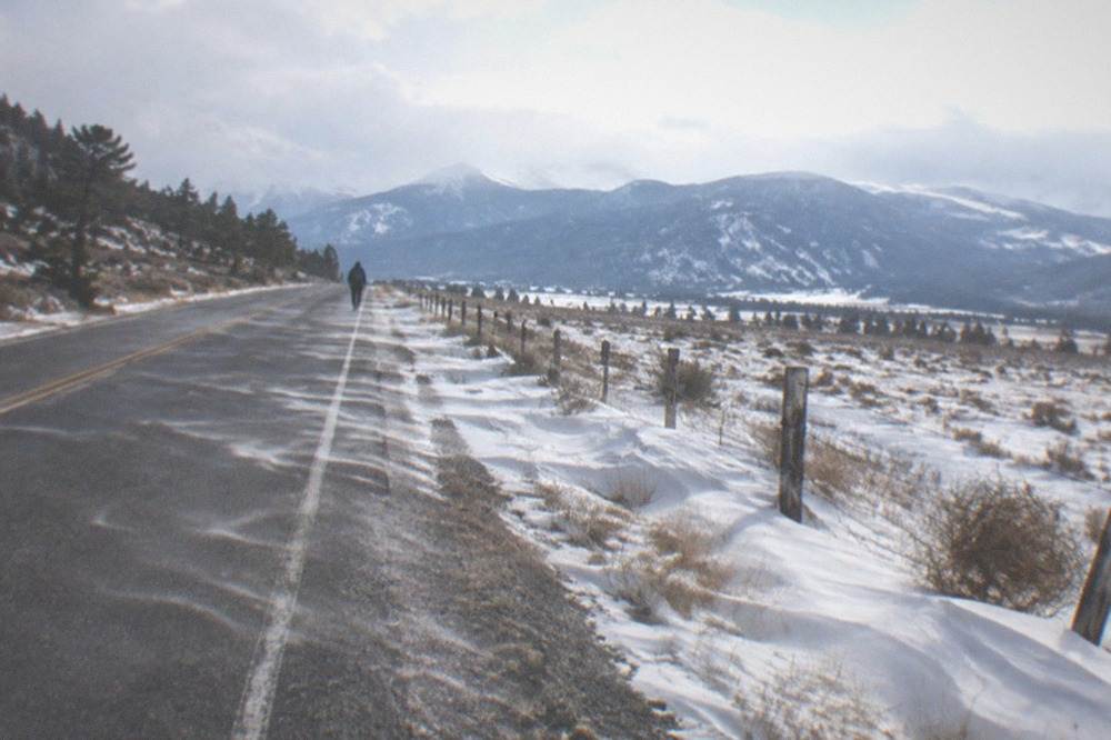 Empty winter highway crossing open snow-dusted plains with distant mountains under a wide sky
