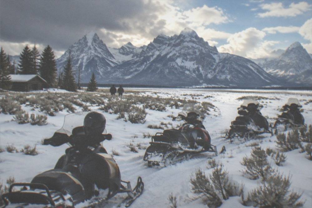Guided snowmobiles parked in a snowy meadow surrounded by tall mountain peaks.