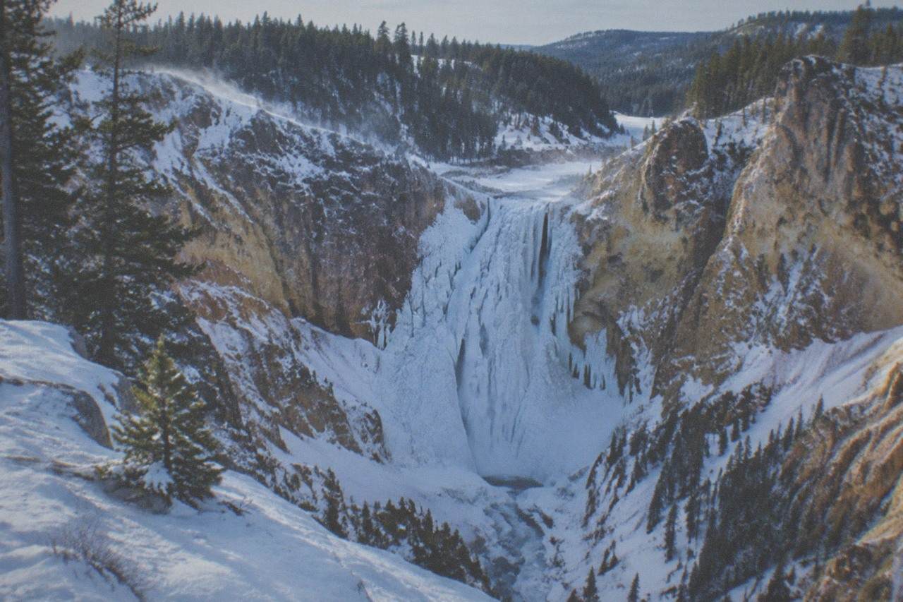 Snow-covered canyon walls and a frozen waterfall under a cold blue sky in a winter mountain landscape