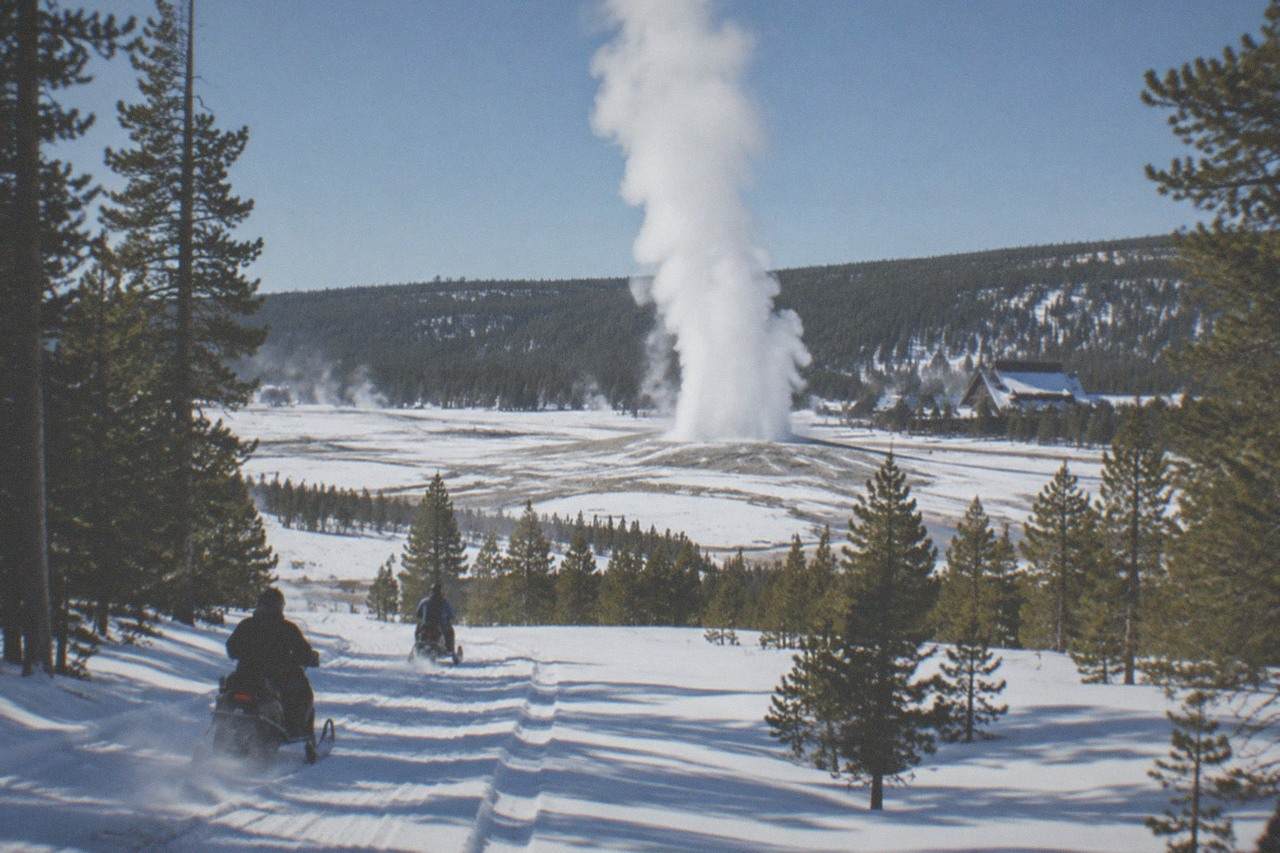 Snow-covered road through Yellowstone with snowmobiles and steam from geothermal features