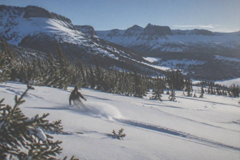 A single snowmobile and rider carving fresh tracks across a wide open snow-covered meadow under a blue sky
