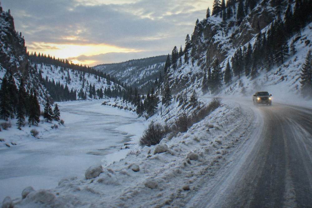A plowed two-lane winter highway following a frozen river between snow-covered canyon walls