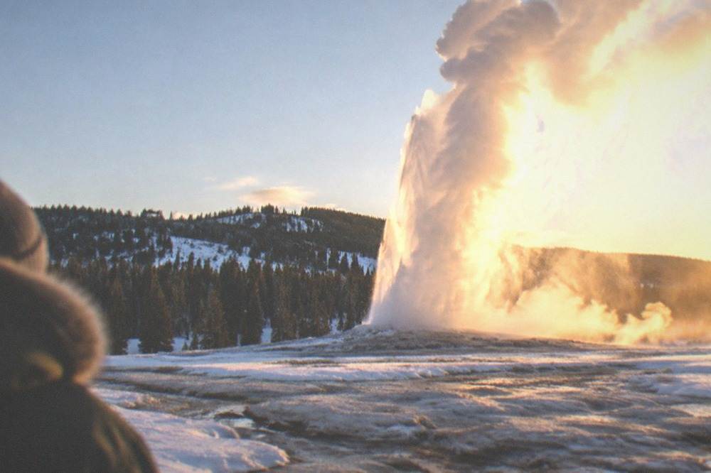 Steam rising from Old Faithful geyser against a clear cold sky above snow-covered ground