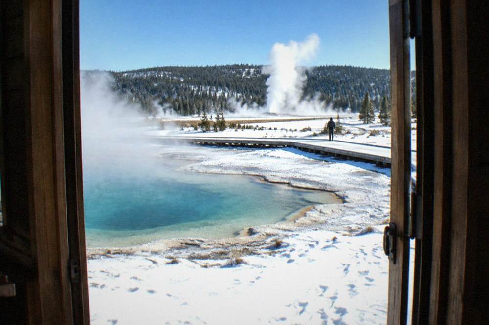 Steam rising from geothermal pools beside a snow-covered boardwalk under a blue winter sky