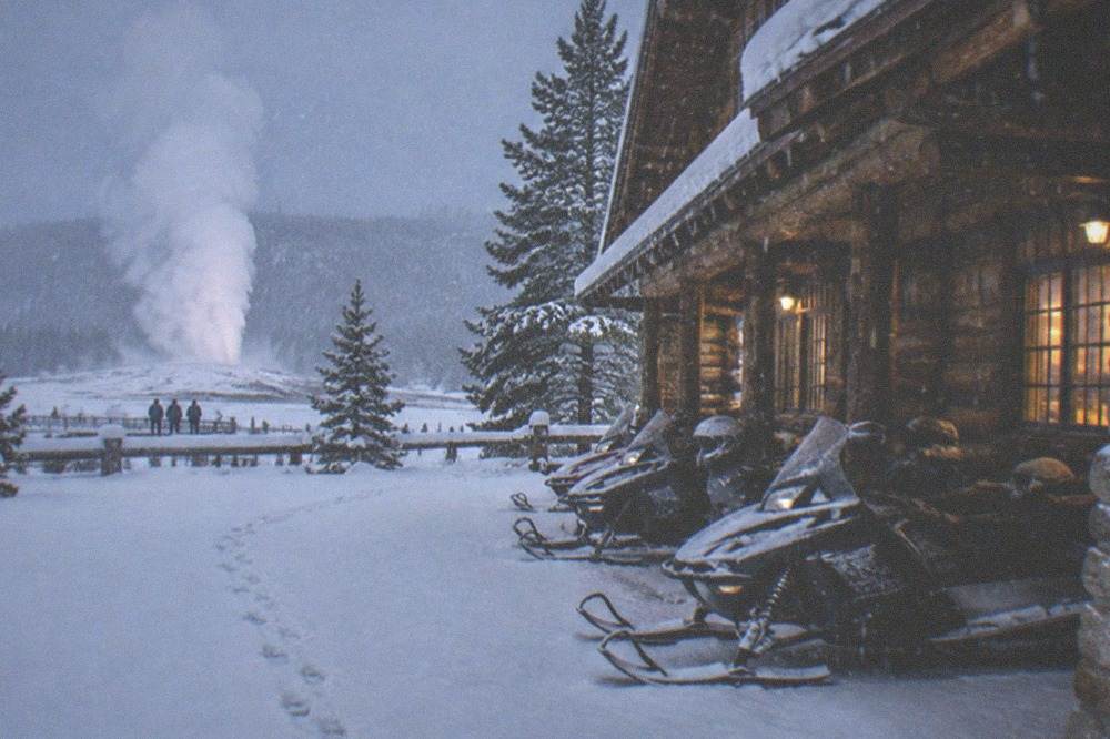 A line of parked snowmobiles outside a rustic log lodge in falling snow