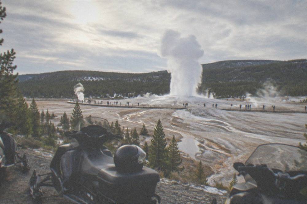 Snowmobiles parked in a row at a scenic overlook with steam rising from distant geothermal pools