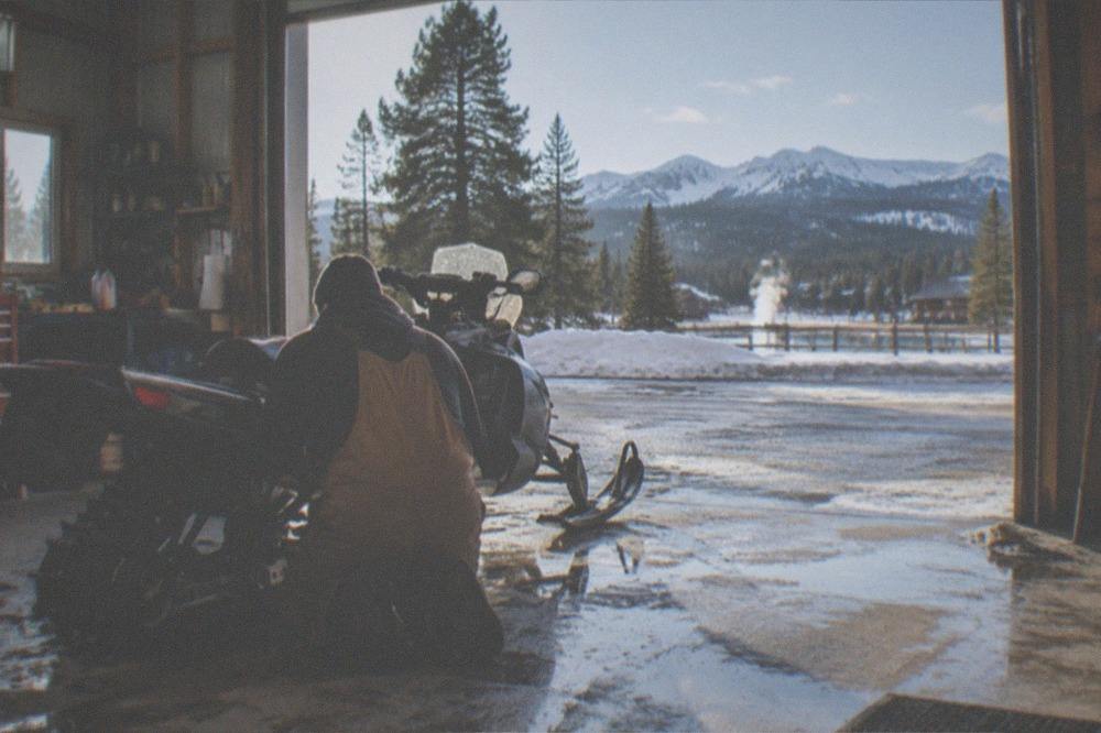 Mechanic checking the track and skis of a snowmobile inside a bright rental garage