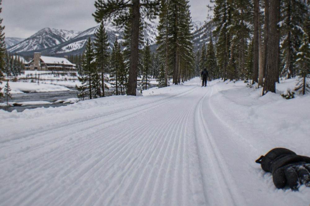 A groomed snowmobile trail winding through snow-covered pine forest toward distant mountains