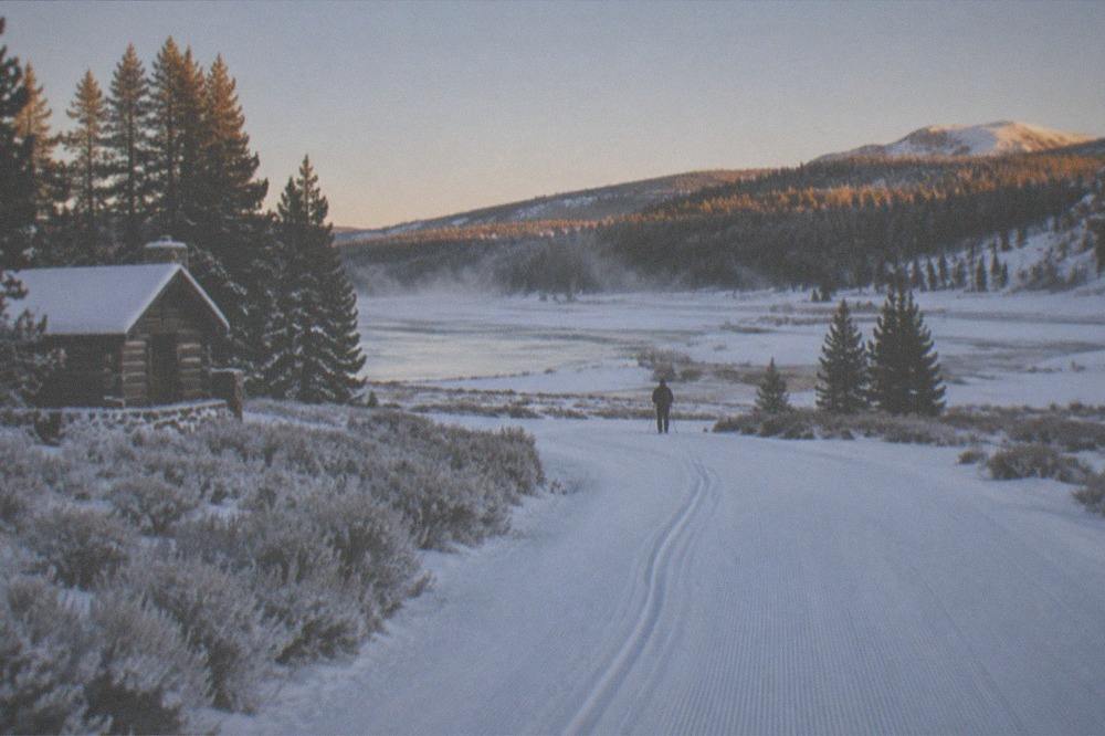 Freshly groomed snowmobile trails crossing open snowy meadow at dawn