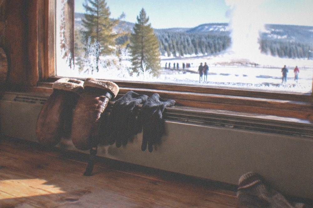 Leather snowmobile mittens and glove liners drying above a baseboard heater next to a wool sock