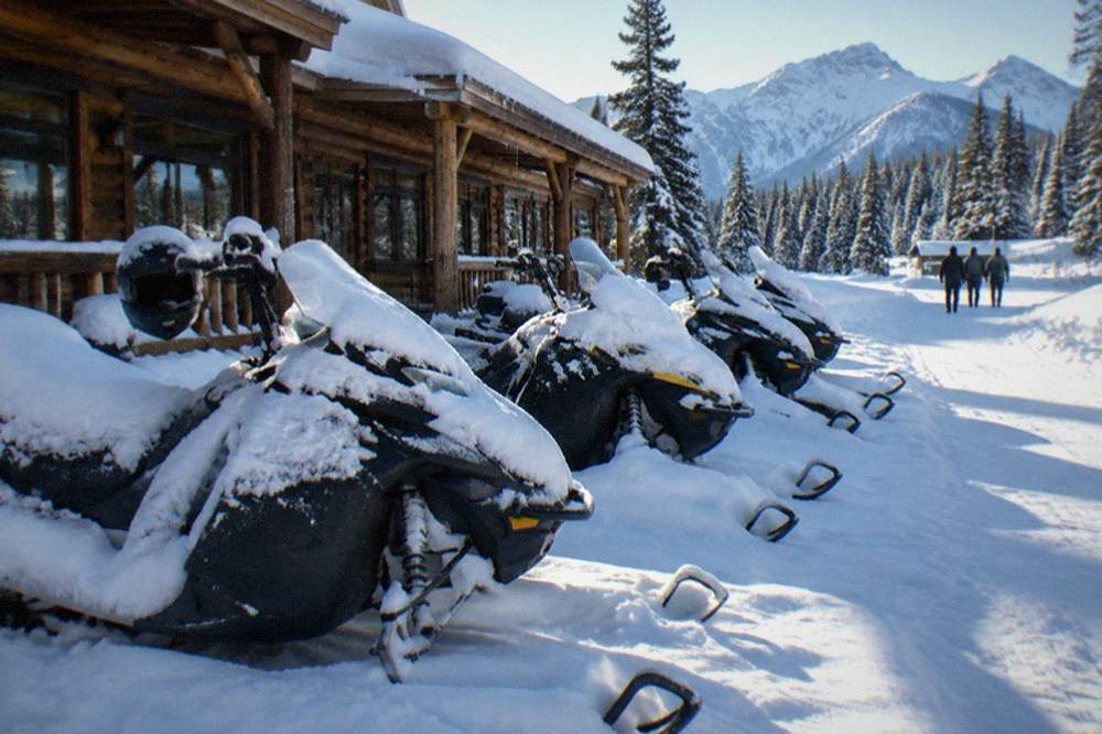 A row of snowmobiles parked in deep snow outside a wooden lodge storefront