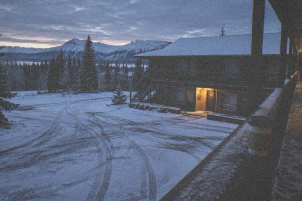 A snow-covered parking lot and dark hotel entrance lit before sunrise