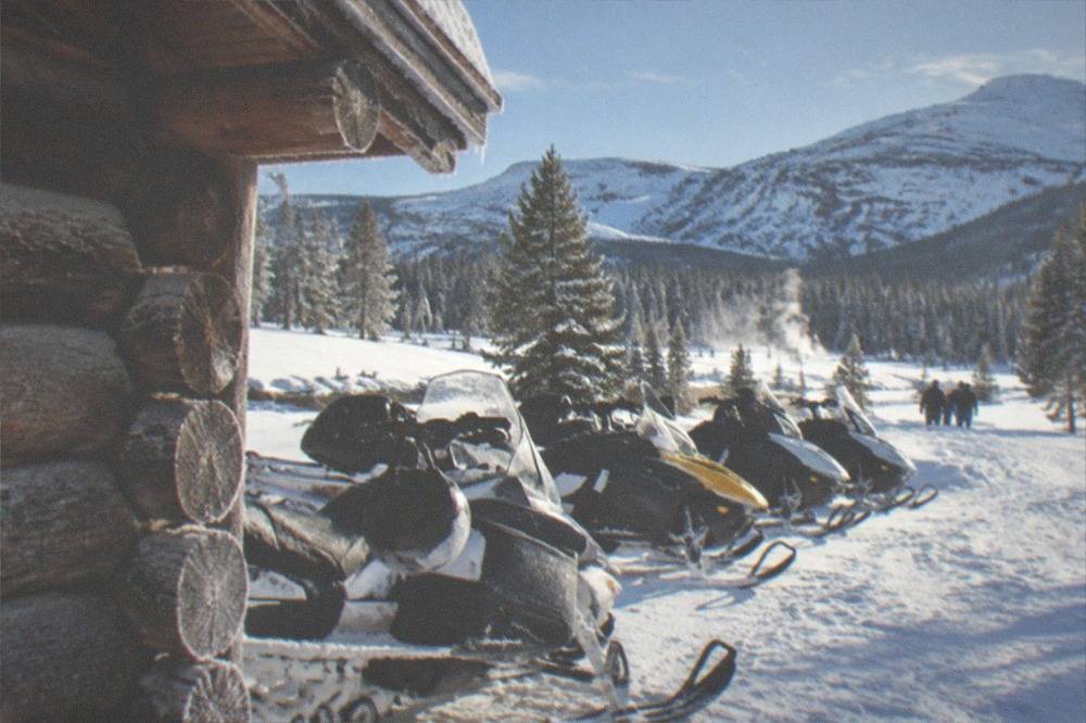 A row of parked snowmobiles outside a warming hut beneath a clear cold sky