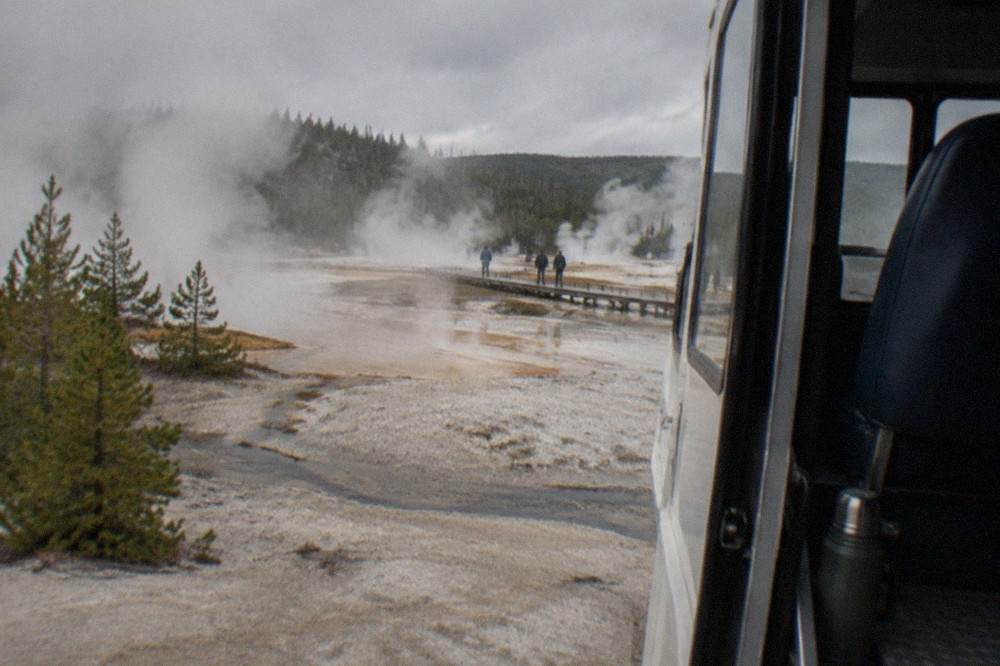 A snowcoach parked on a snow-covered road beside steaming geothermal pools