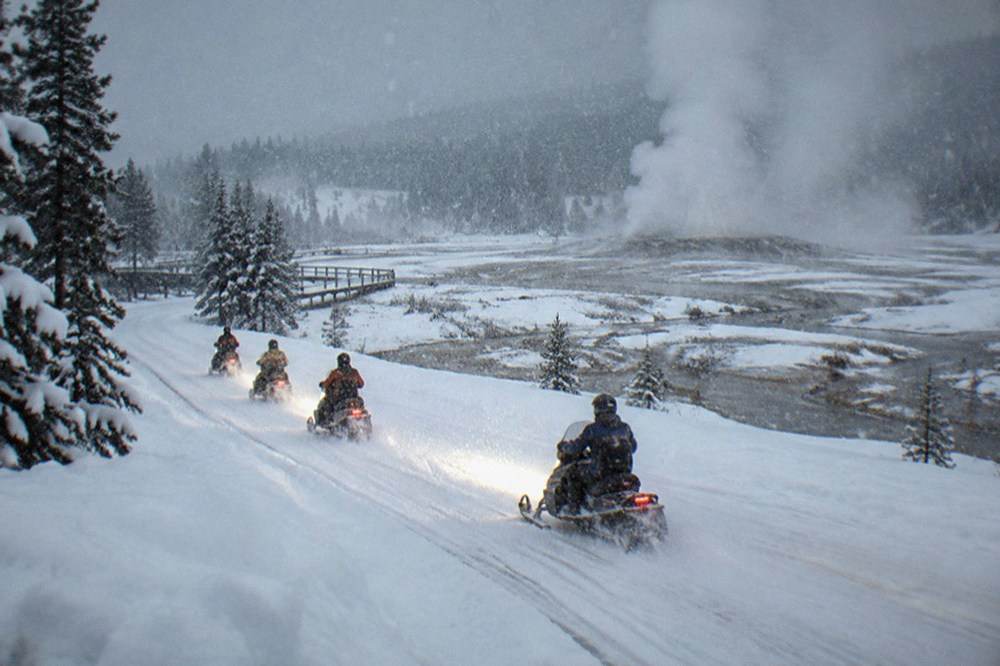 A small group of snowmobiles traveling single file along a groomed road in falling snow