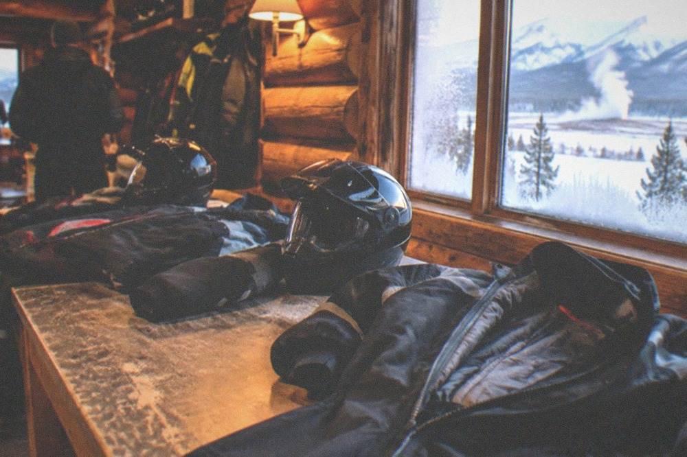 Insulated snowmobile suits and helmets laid out on a bench before a tour departure