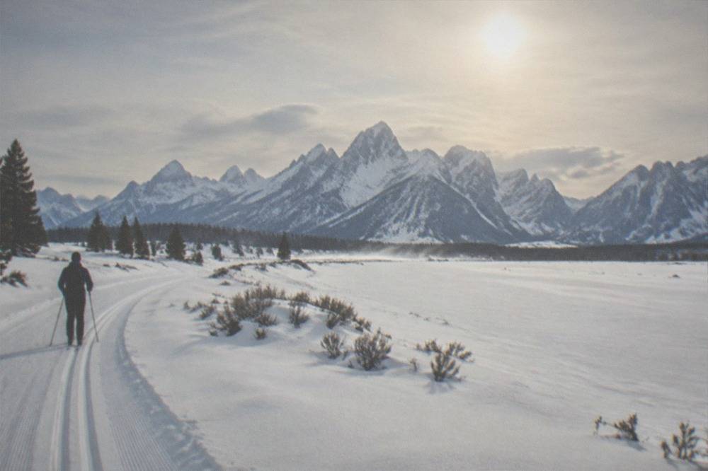 Wide snowy meadow with mountain peaks and a groomed trail through deep powder