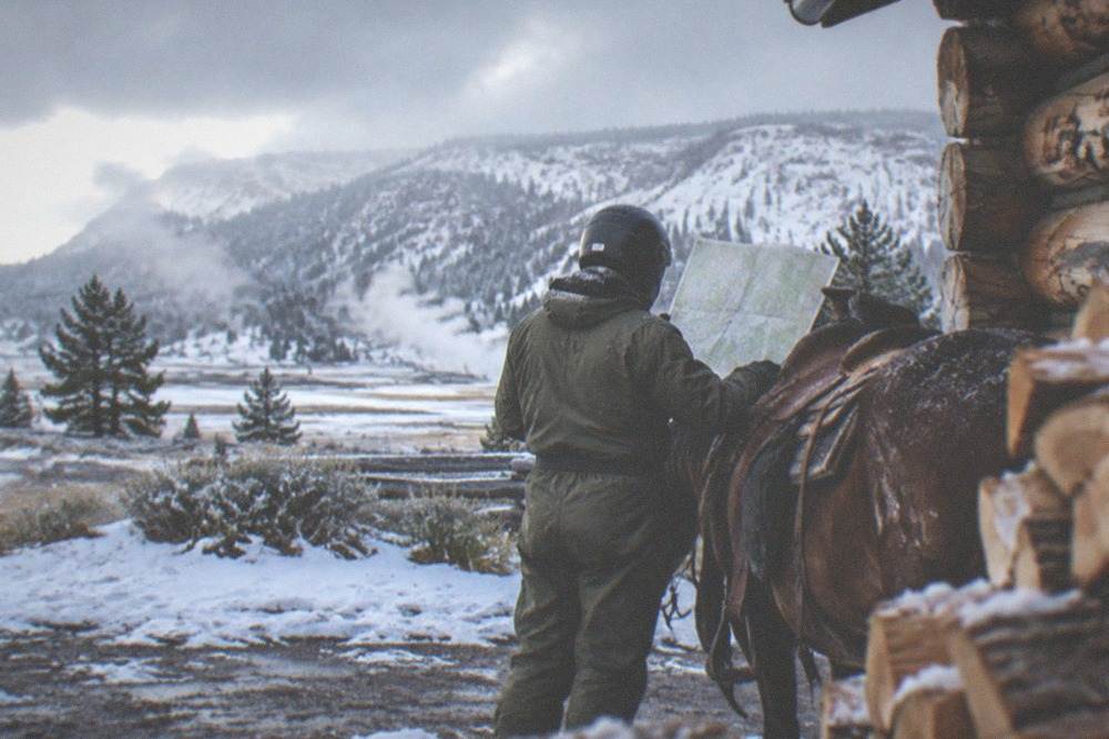 Rider in an insulated snowmobile suit and full-face helmet checking a frozen trail map at a winter warming hut
