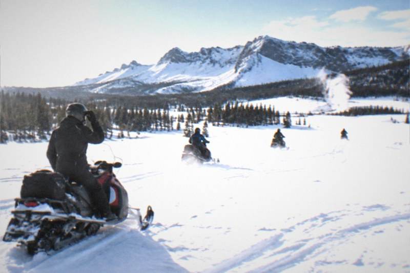 Guided snowmobile group crossing a snow meadow in Bridger-Teton National Forest